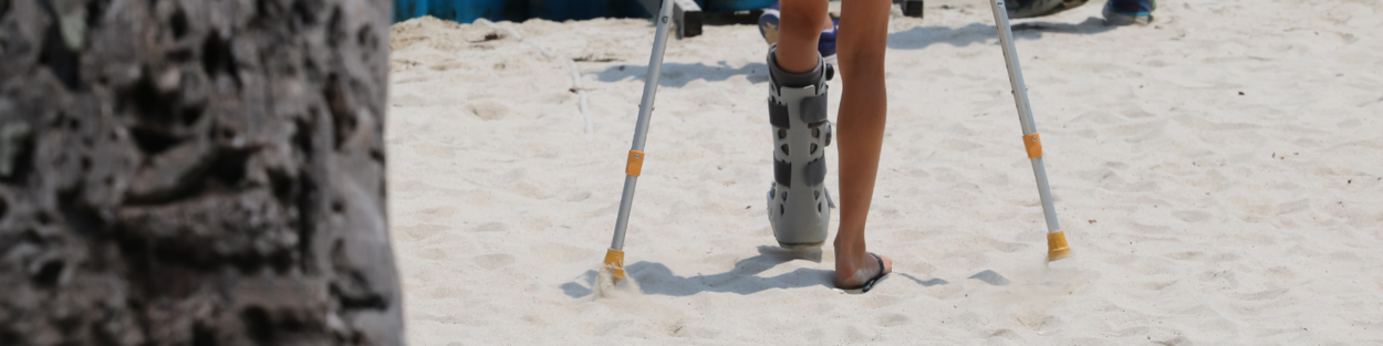 Dame met been in het gips loopt op krukken over het strand
